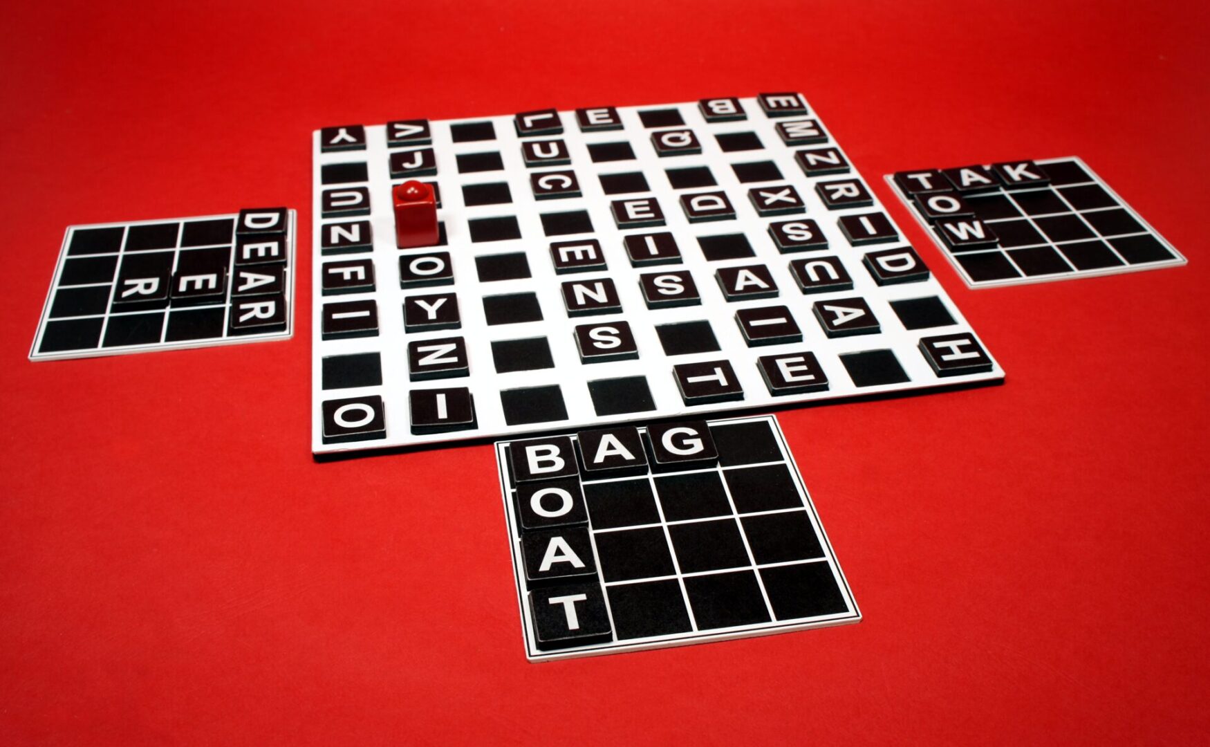 A word puzzle game with black and white letter tiles on a red surface.